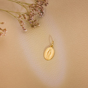 Medalla de la Virgen Milagrosa, en oro de ley 18k de 16x10 mm, colgando de una cadena sobre fondo claro