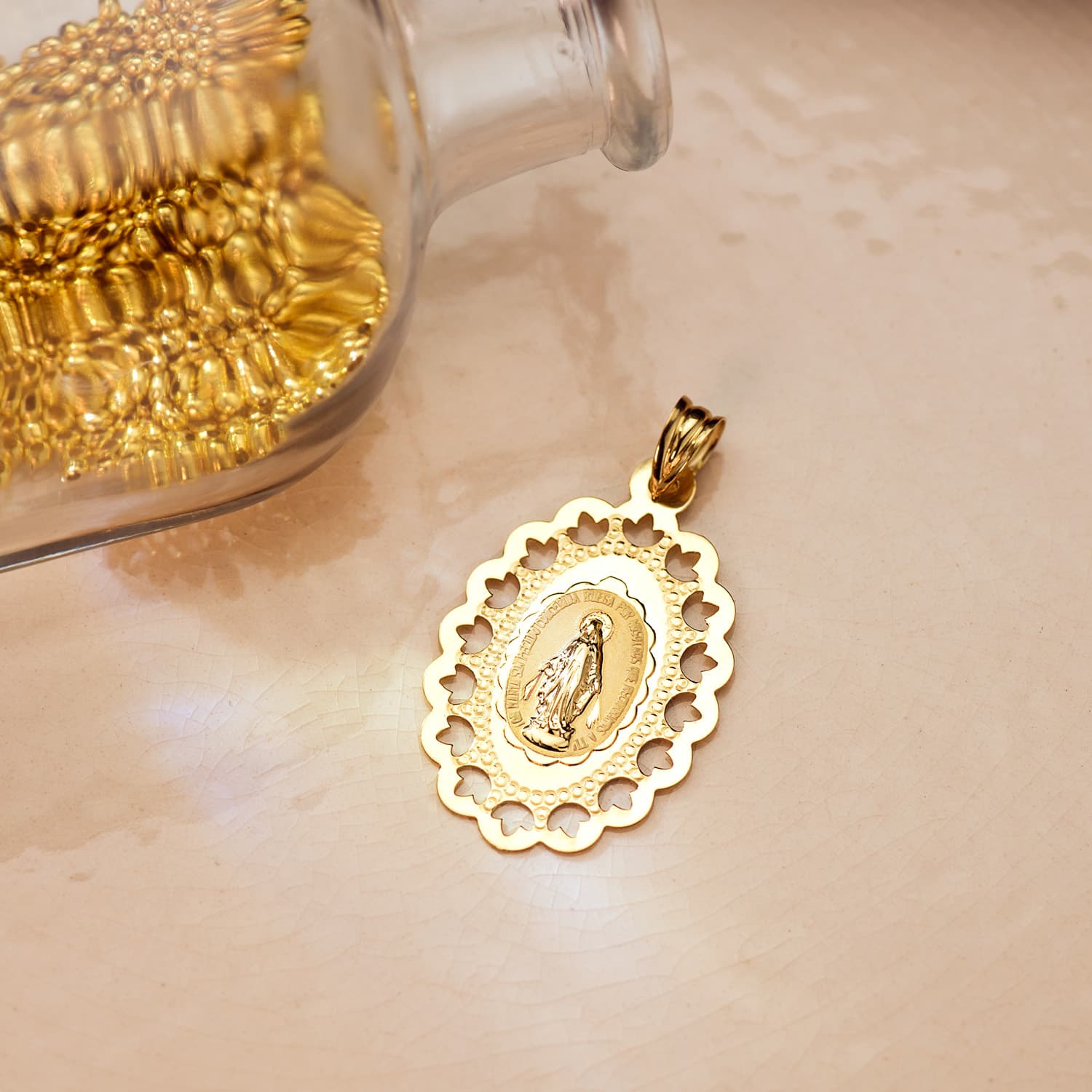 Medalla de la Virgen Milagrosa en oro de ley 18k de 33x22 mm sobre una superficie clara junto a un frasco de cristal