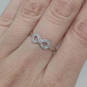 Anillo fino de oro blanco de ley 18k con circonitas en forma de infinito mano